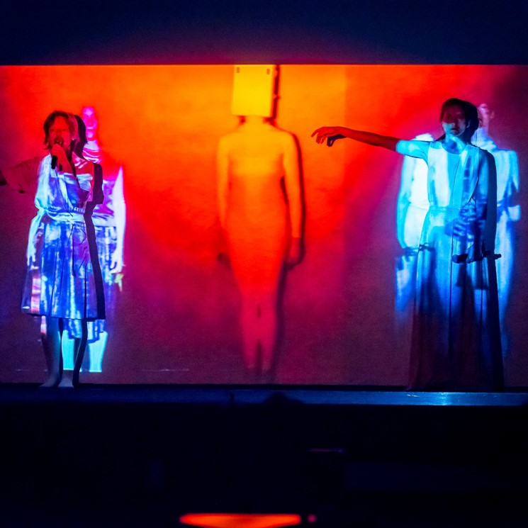 Kadr z utworu audiowizualnego, dwie performerki stoją na tle projekcji